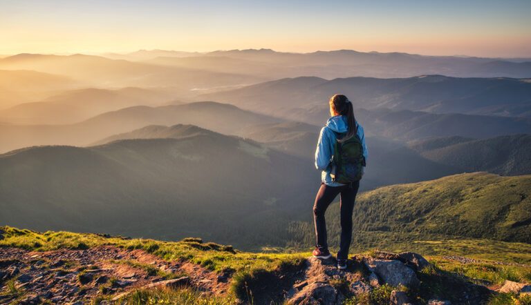 Cloud-Komplexität meistern: Mit Fujitsu Uvance Hybrid IT Services // A woman standing on a rock formation looking at mountains at sunrise