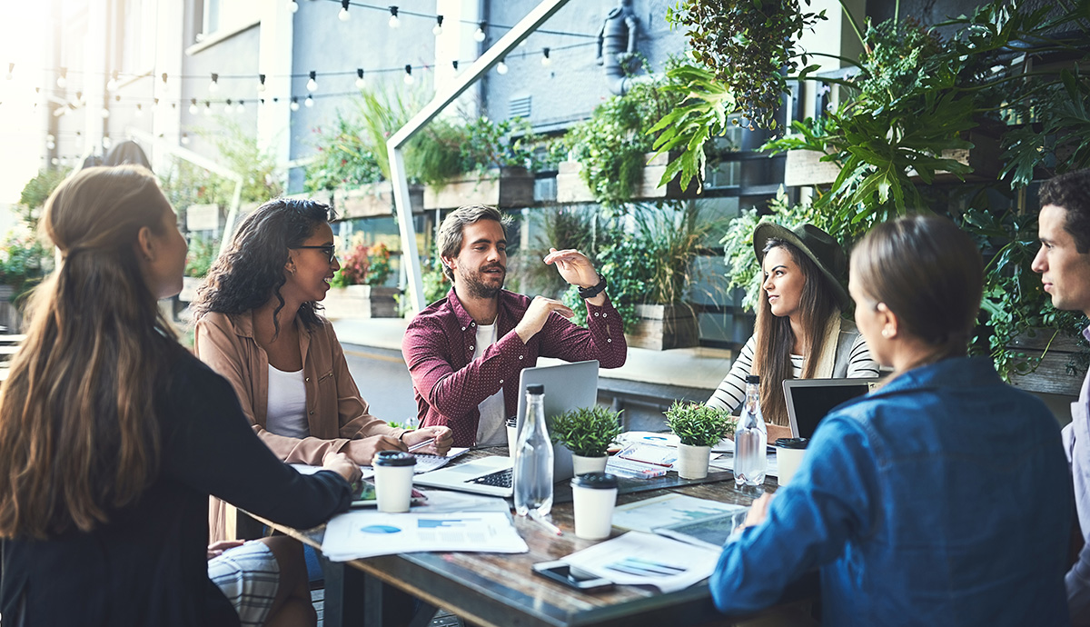 Wandel beginnt im Führungsverhalten // A diverse creative team meeting around a table at a coffee shop.