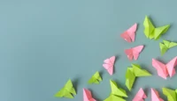 Vom Hype zur Umsetzung: Drei Thesen als Wegweiser für erfolgreiche KI-Projekte // Pink and green origami butterflies on light blue background