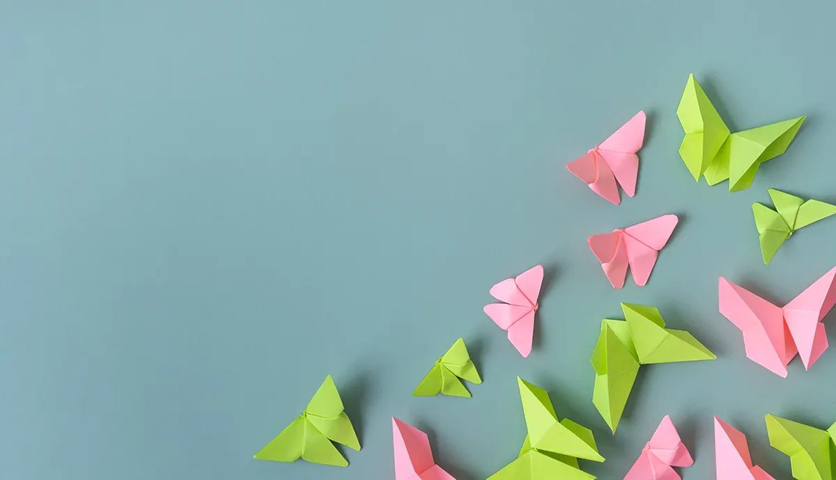 Vom Hype zur Umsetzung: Drei Thesen als Wegweiser für erfolgreiche KI-Projekte // Pink and green origami butterflies on light blue background