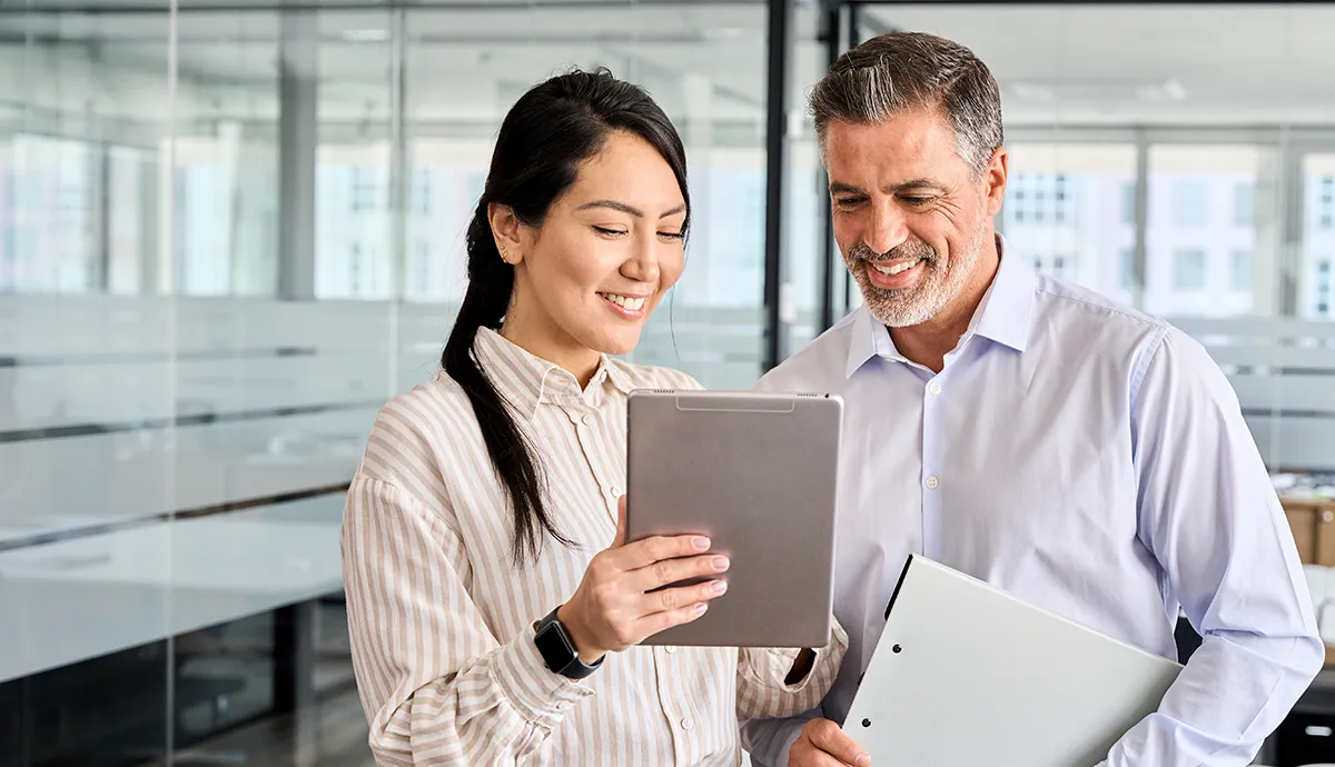 Wie KI Low-Code grundlegend erweitert // Senior White man and young Asian woman looking at a digital tablet at the office